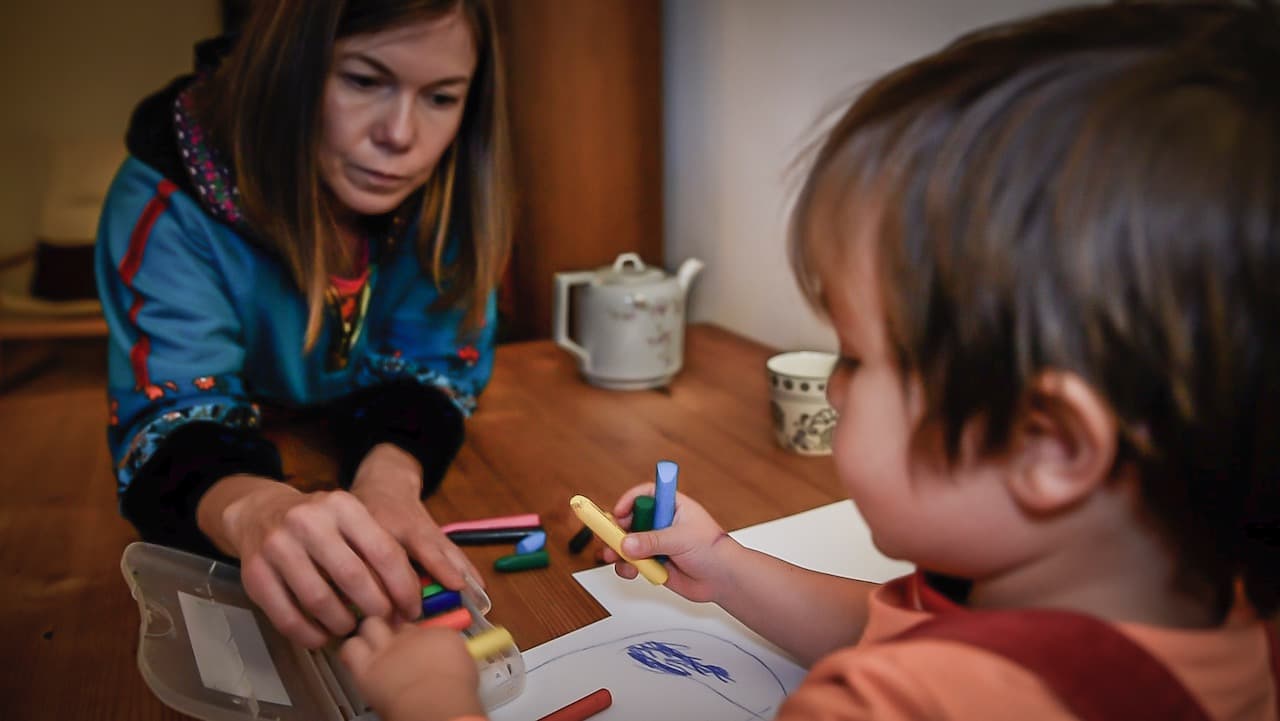 A young woman helps a young child draw with crayons