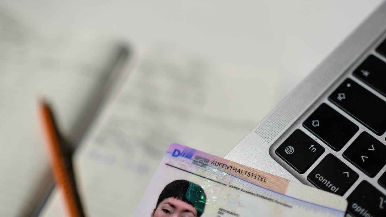 A residence permit card in the foreground, with parts of a laptop and a pencil and a notepad visible in the background