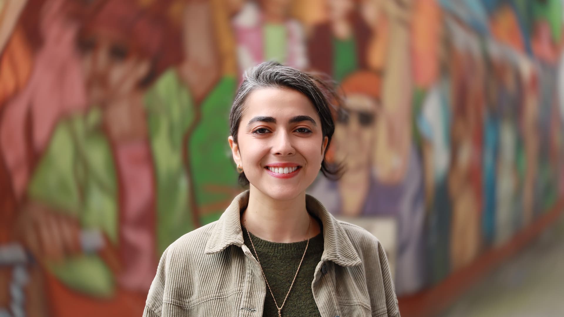 Community-Managerin Su steht vor bunter Wand und lächelt.