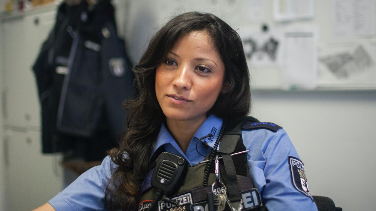 A young police woman is sitting in her uniform at a table in a police office.