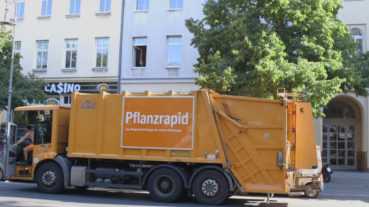 Auf dem Bild sieht man ein orangenes Müllauto auf einer Straße.