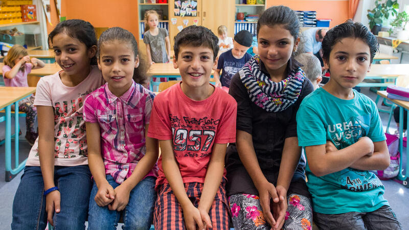 Das Bild zeigt fünf Kinder auf einem Tisch sitzend in einem Klassenzimmer.